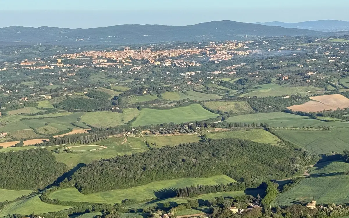 A balloon drifting low over rolling Tuscan hills with cypress trees and farm buildings