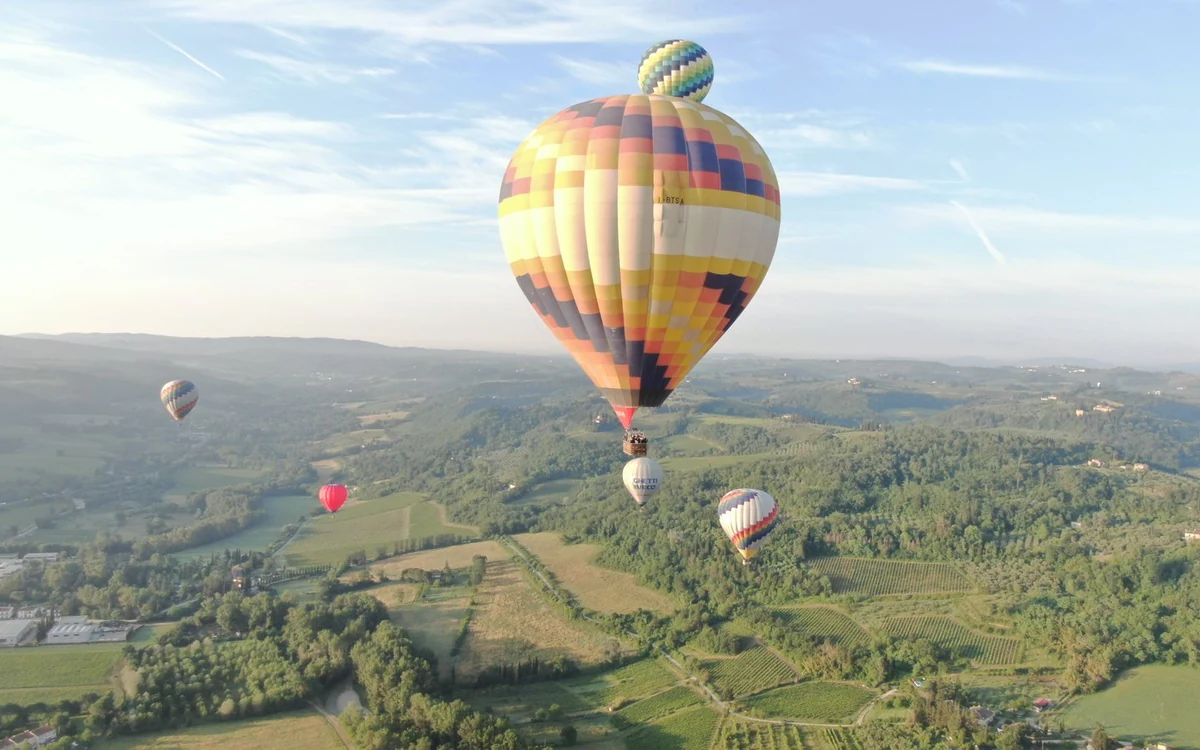 A large striped balloon over wooded Tuscan hills with four smaller balloons around it
