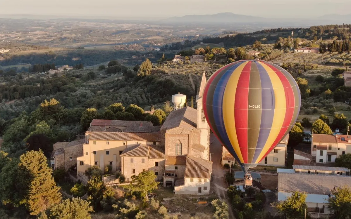 A balloon drifting beside a stone hill village with a church tower, hills fading behind it