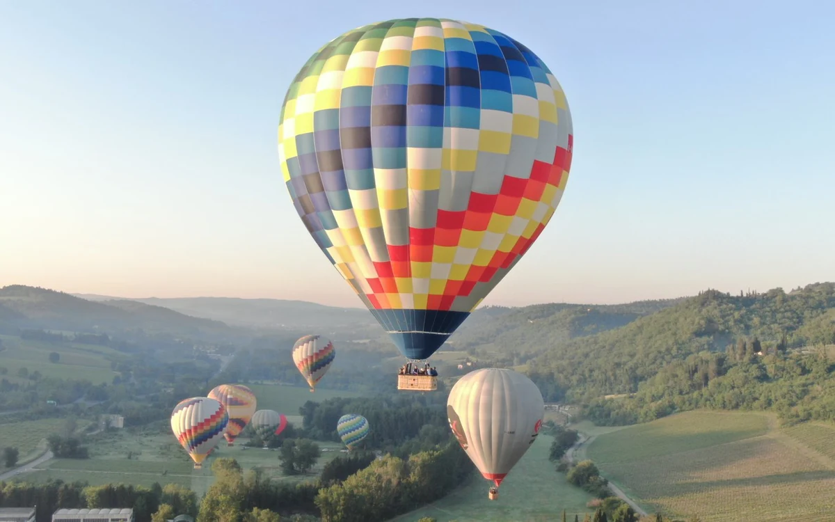 A hot air balloon drifting above the hills and cypress trees of Tuscany at sunrise