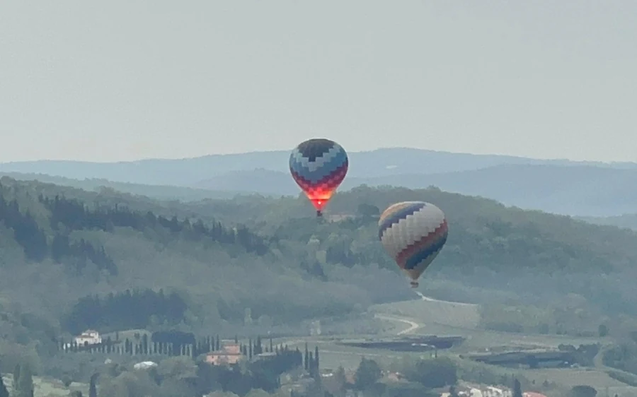 Two balloons hanging over hazy wooded ridges, the nearer one with its burner lit