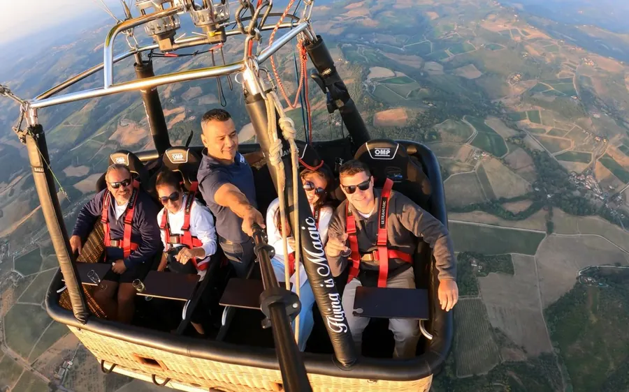Passengers strapped into a seated balloon basket high above a patchwork of fields