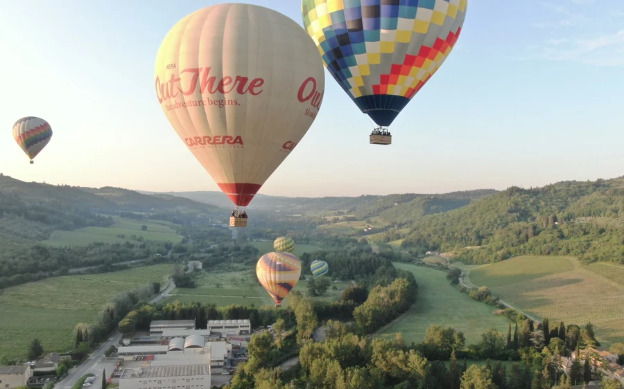 Several balloons over green valleys and vineyards in early morning light