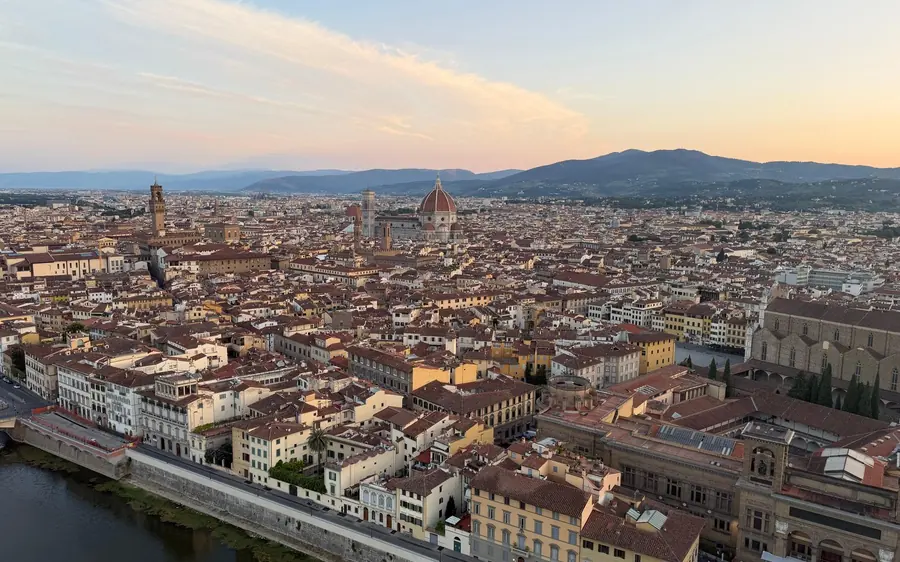 Florence from above in early light, the Duomo and the tower rising over tiled roofs beside the river